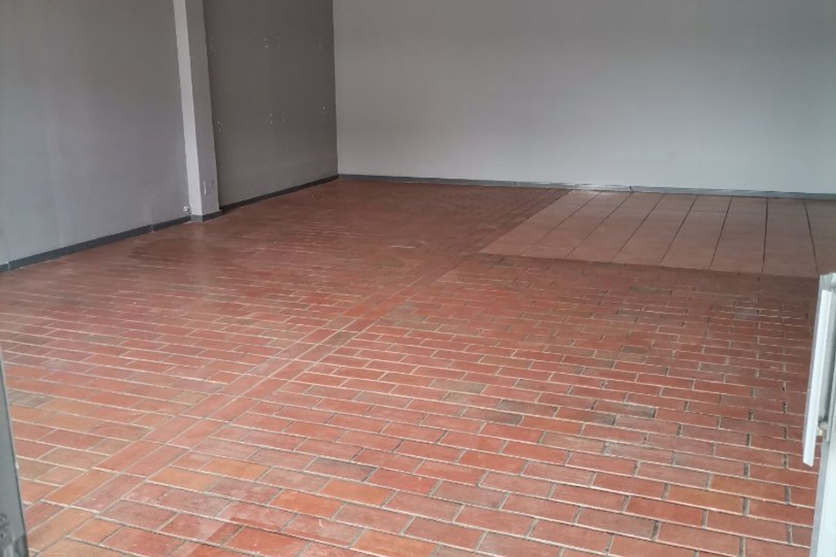 An empty, open-plan living area featuring a mix of terracotta and ceramic tile flooring with grey painted walls.