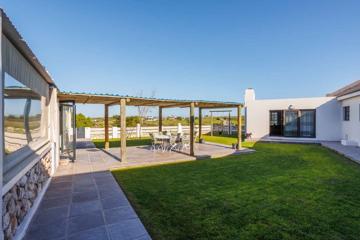 A spacious rear garden featuring a paved patio area with a timber-framed pergola, well-maintained lawn, and direct access to the main dwelling.