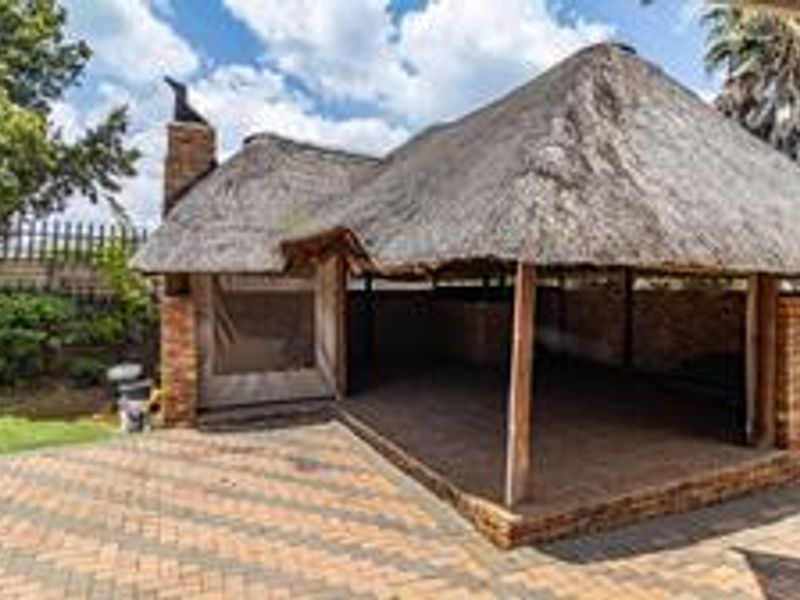 A spacious outdoor patio area featuring a traditional thatch roof, brick construction, and paved flooring, ideal for outdoor entertaining.
