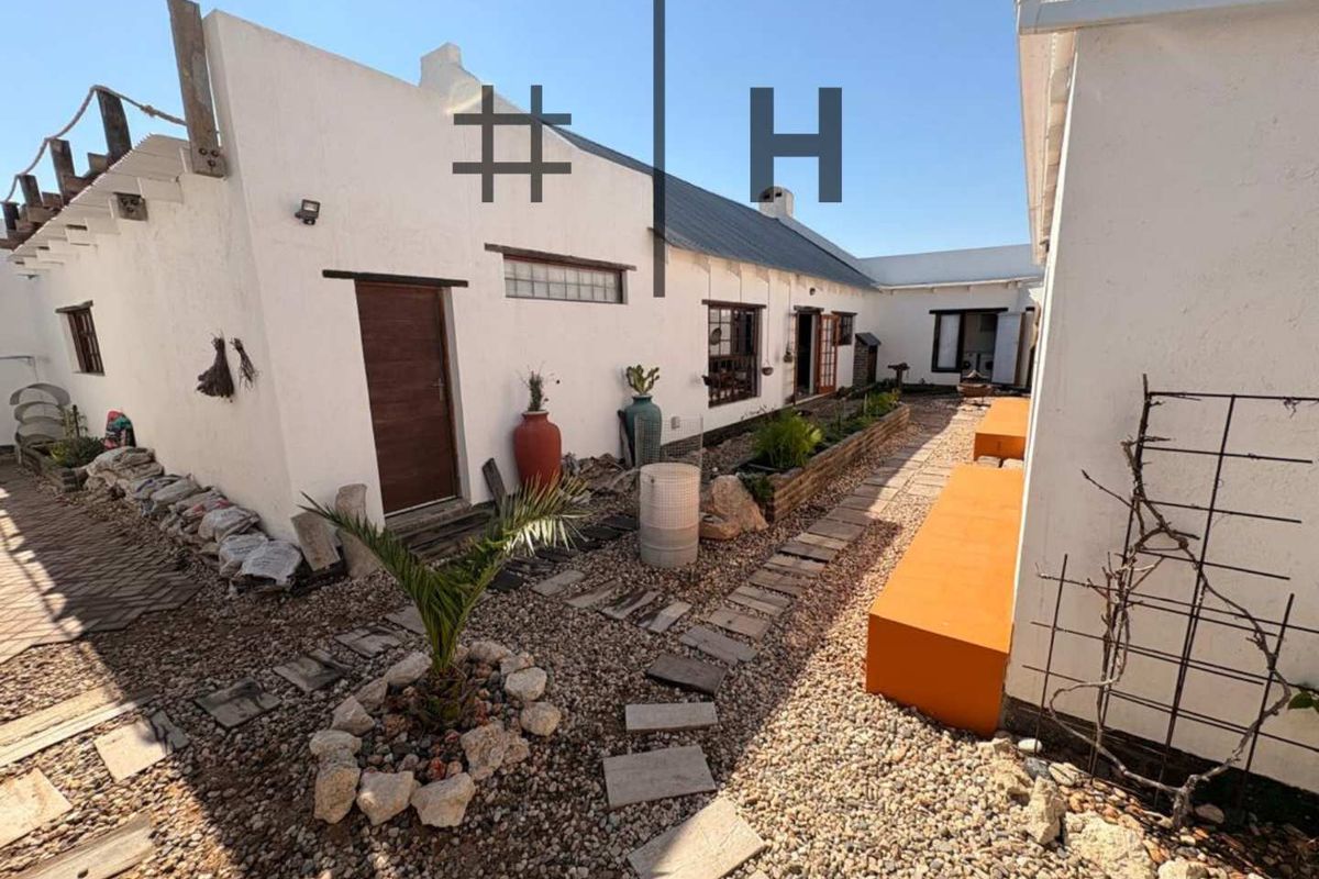 A rustic rear courtyard featuring gravel pathways, stone pavers, and built-in masonry seating, connecting multiple sections of the property with a charming, weathered aesthetic.