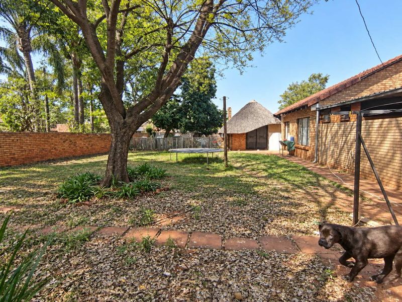 Spacious rear garden featuring a brick boundary wall, paved walkway, and a traditional thatched lapa structure.