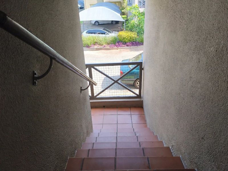 Exterior staircase with tiled steps, metal handrail, and security gate leading to the property entrance.