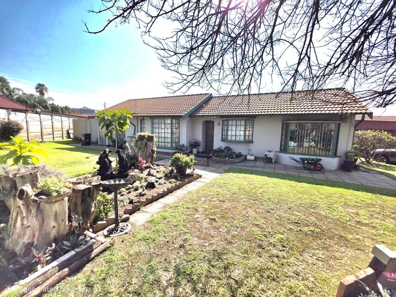 Rear view of a single-story house featuring a tiled roof, bay windows, a paved patio area, and an established garden.