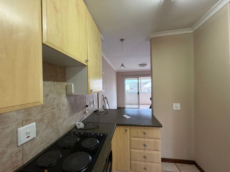 Compact kitchen featuring laminate cabinetry, dark countertops, and an electric hob, with an open flow toward a sliding door leading to a balcony.