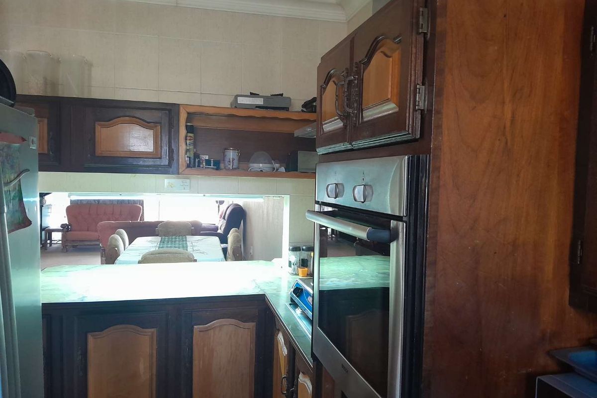 A dated kitchen featuring dark wood cabinetry, built-in oven, and a pass-through window overlooking the adjacent living and dining area.