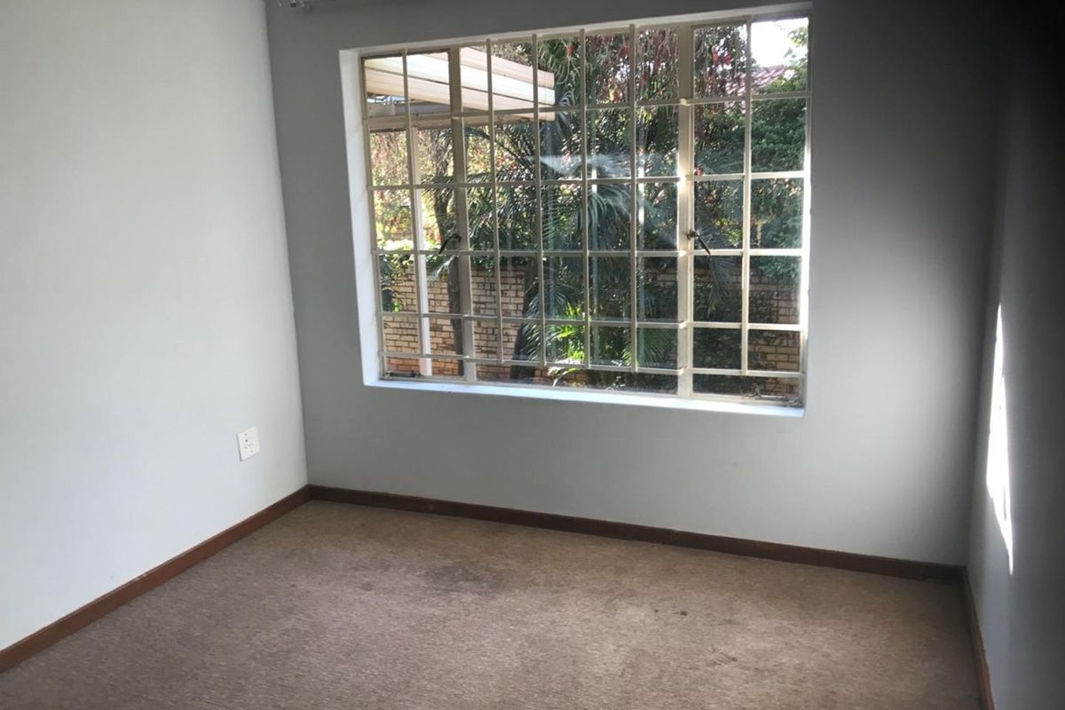 An empty bedroom featuring carpeted flooring, neutral walls, and a large window fitted with security burglar bars.