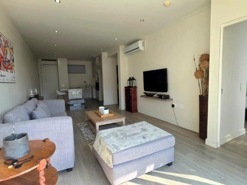 Open-plan living area featuring laminate flooring, recessed lighting, and a split-system air conditioner, seamlessly connecting to the kitchen and adjacent bedroom.