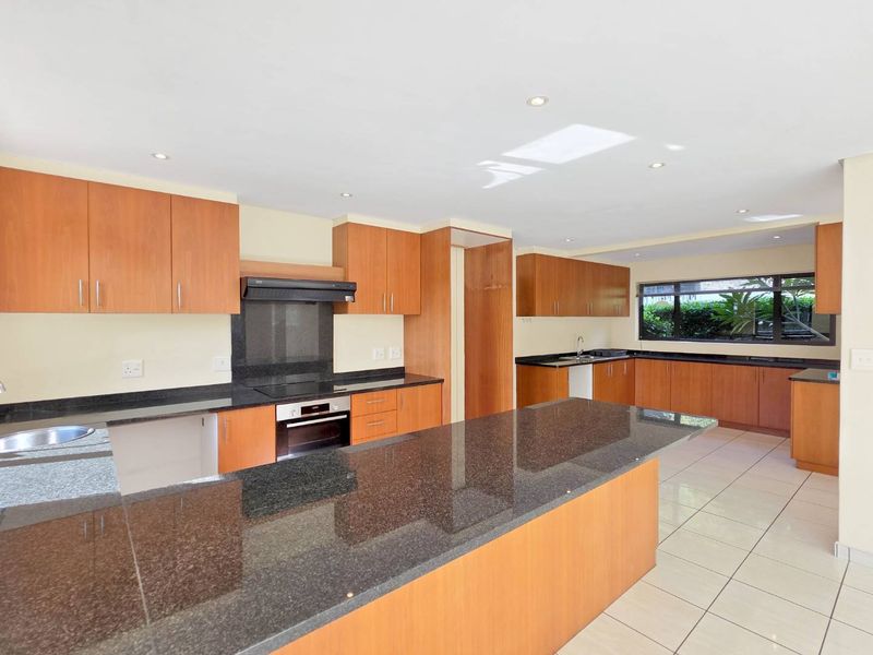 Spacious kitchen featuring granite countertops, a large central island, built-in oven, extractor fan, and ample wooden cabinetry with tiled flooring.