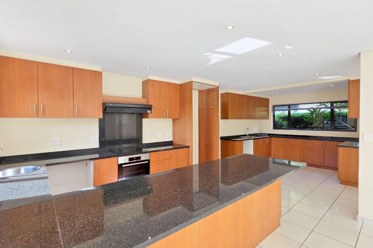 Spacious kitchen featuring granite countertops, a large central island, built-in oven, extractor fan, and ample wooden cabinetry with tiled flooring.