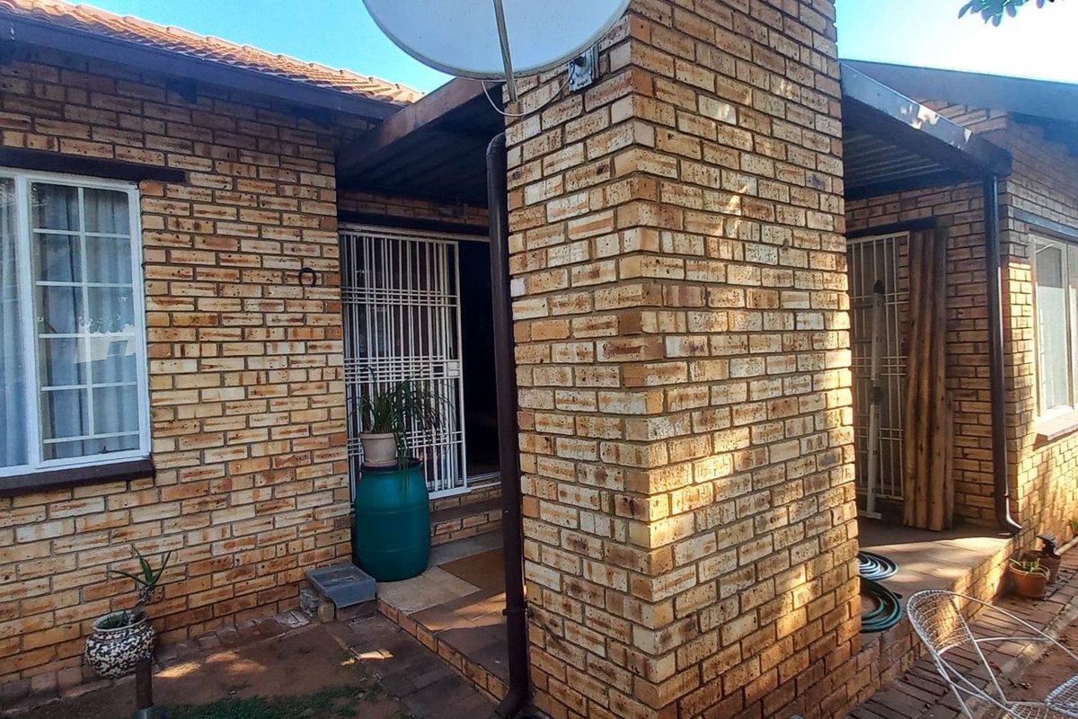 Exterior view of a face-brick townhouse featuring a covered patio area, security gates, and a satellite dish mounted on the chimney structure.