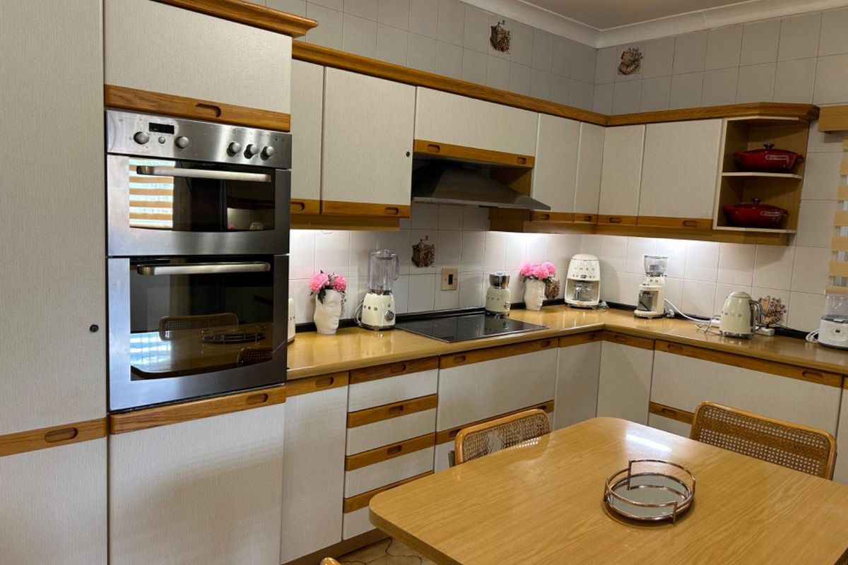 A functional kitchen featuring built-in cabinetry, a double wall oven, an integrated extractor fan, and a ceramic cooktop with tiled splashbacks.