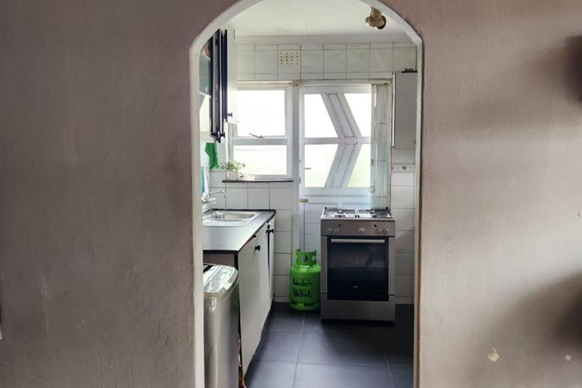 A view through an arched doorway into a functional kitchen featuring tiled flooring, built-in cabinetry, and a freestanding oven.