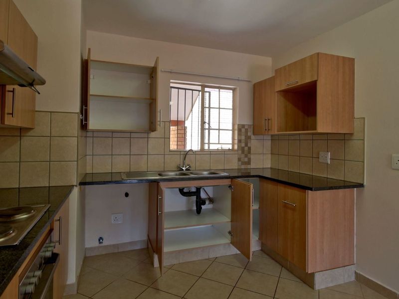 A functional kitchen featuring laminate cabinetry, granite countertops, a double sink, and built-in cooking appliances, currently requiring minor repairs to the under-sink cabinetry.