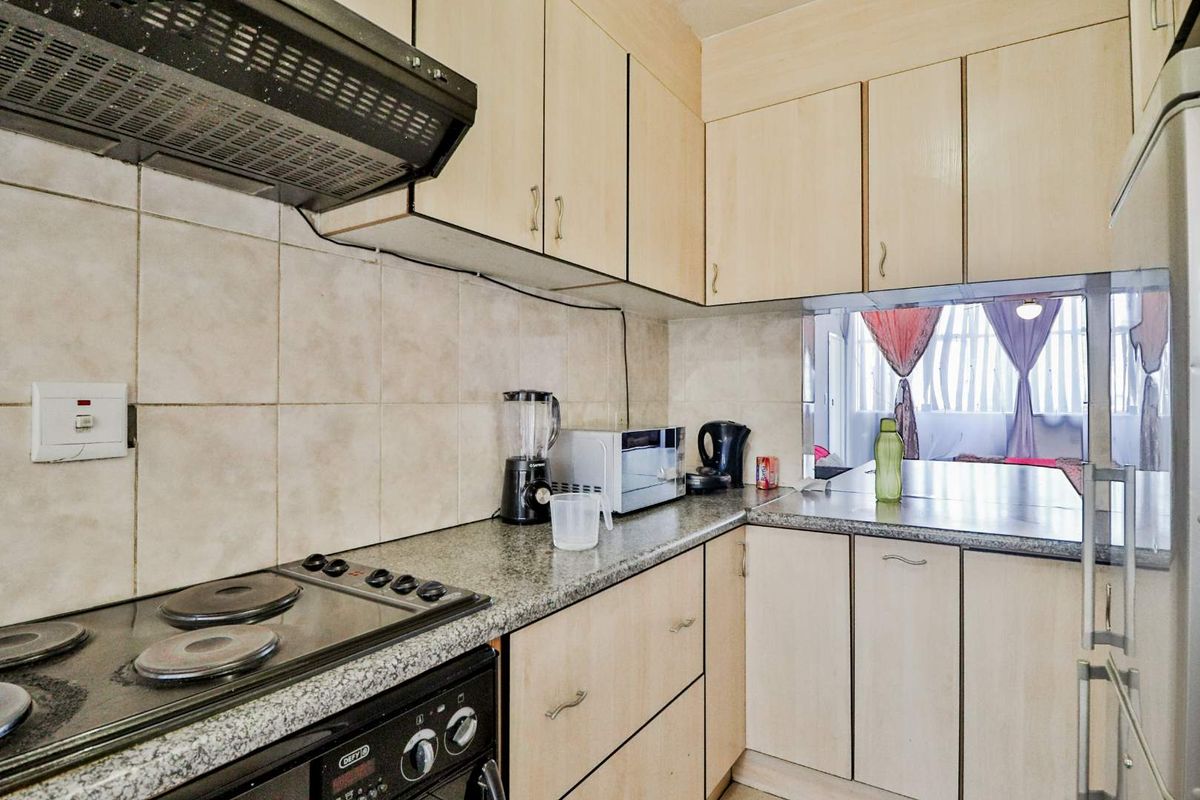 Compact kitchen featuring light wood-finish cabinetry, granite-look countertops, a built-in stove with extractor fan, and a tiled backsplash with a convenient serving hatch.