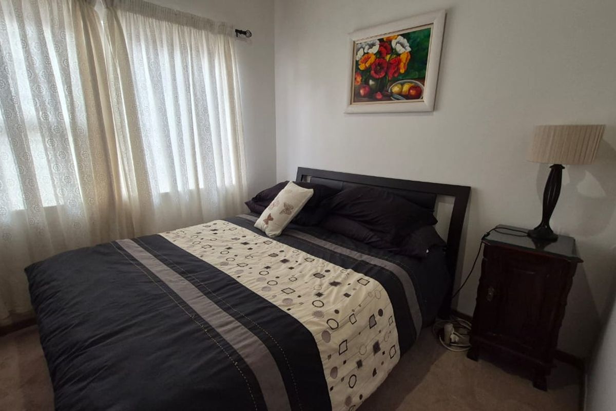 A cozy bedroom featuring neutral wall tones, carpeted flooring, and natural light filtering through window curtains.