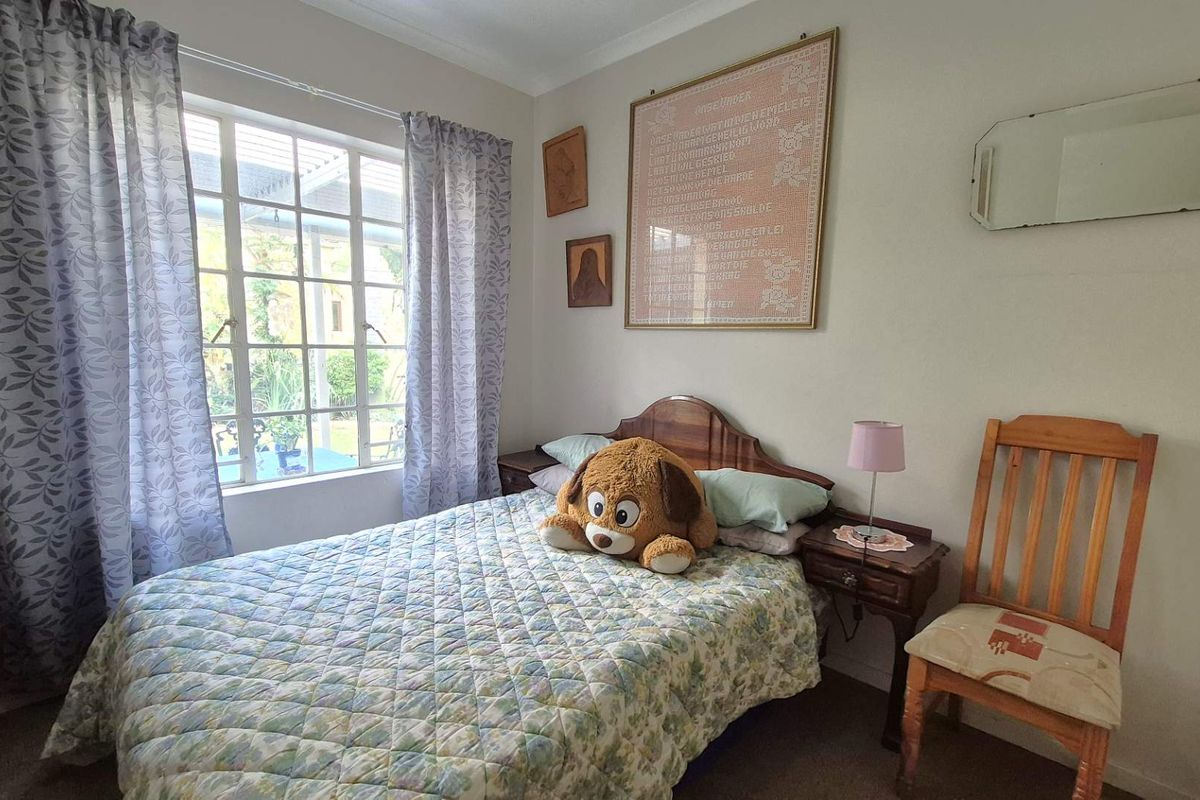 A cozy bedroom featuring a large window with garden views, neutral walls, and carpeted flooring.