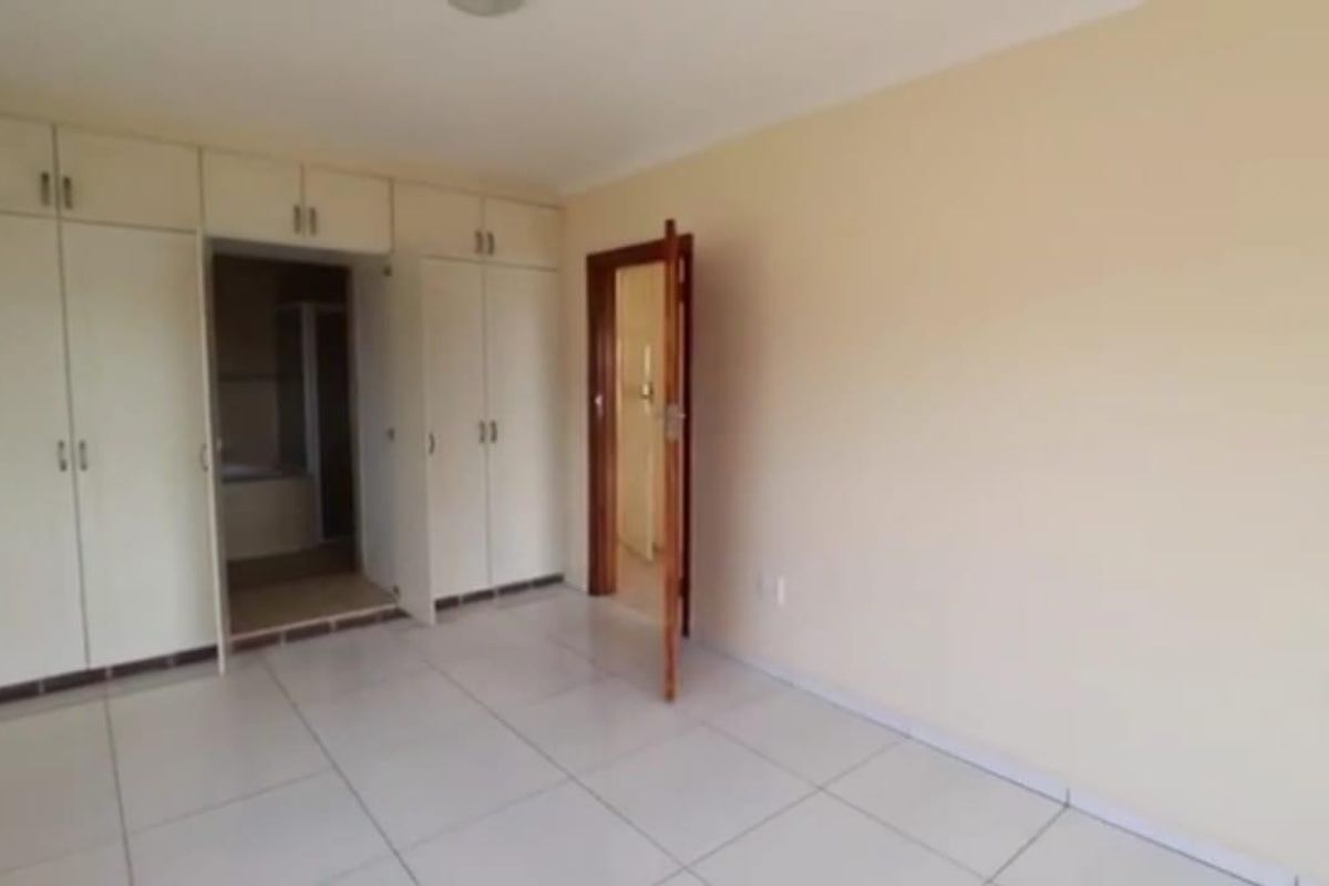 A vacant bedroom featuring neutral walls, tiled flooring, and extensive built-in cupboard storage with direct access to an adjoining bathroom.