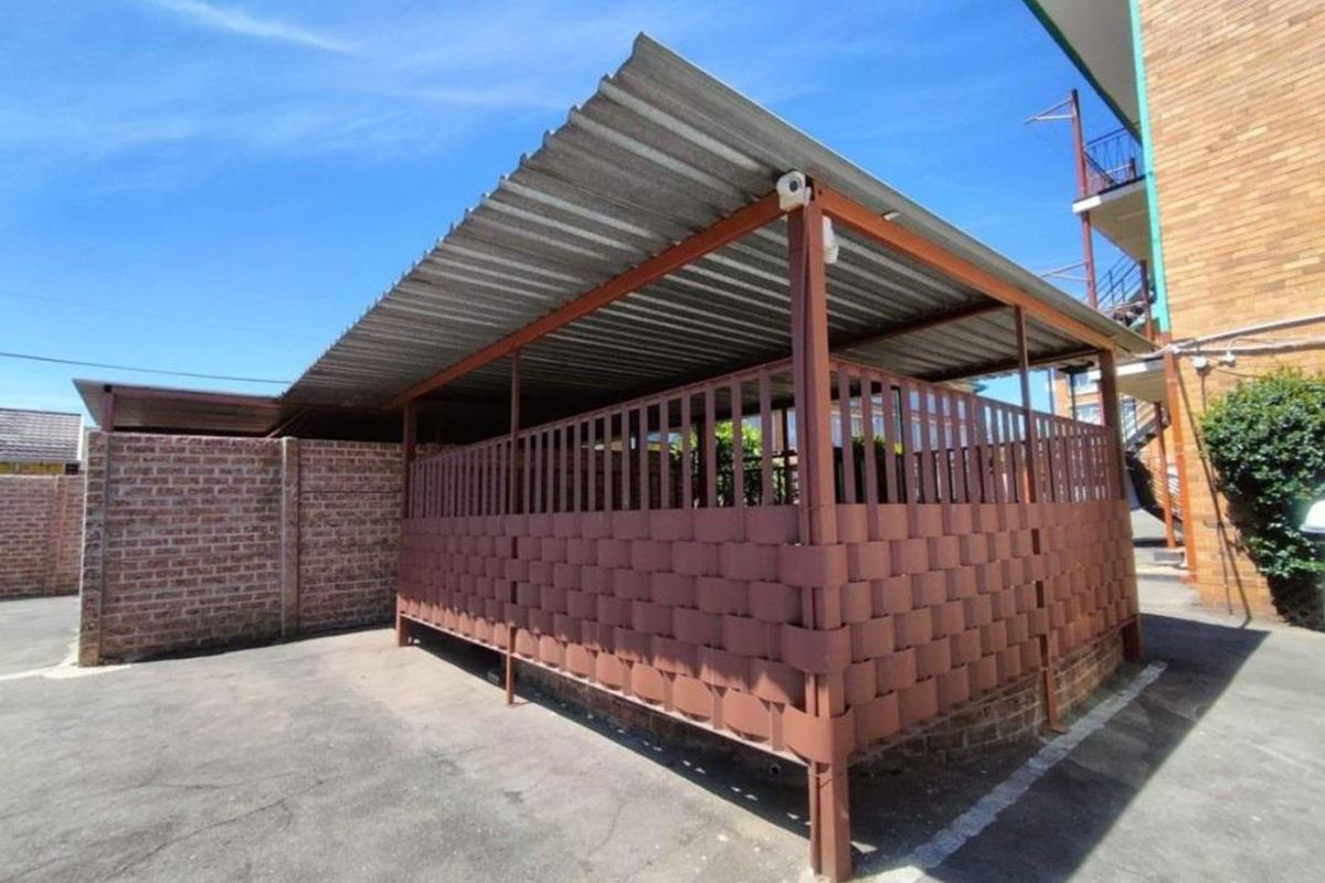 A covered outdoor parking or utility area featuring a corrugated metal roof and a decorative metal privacy screen.