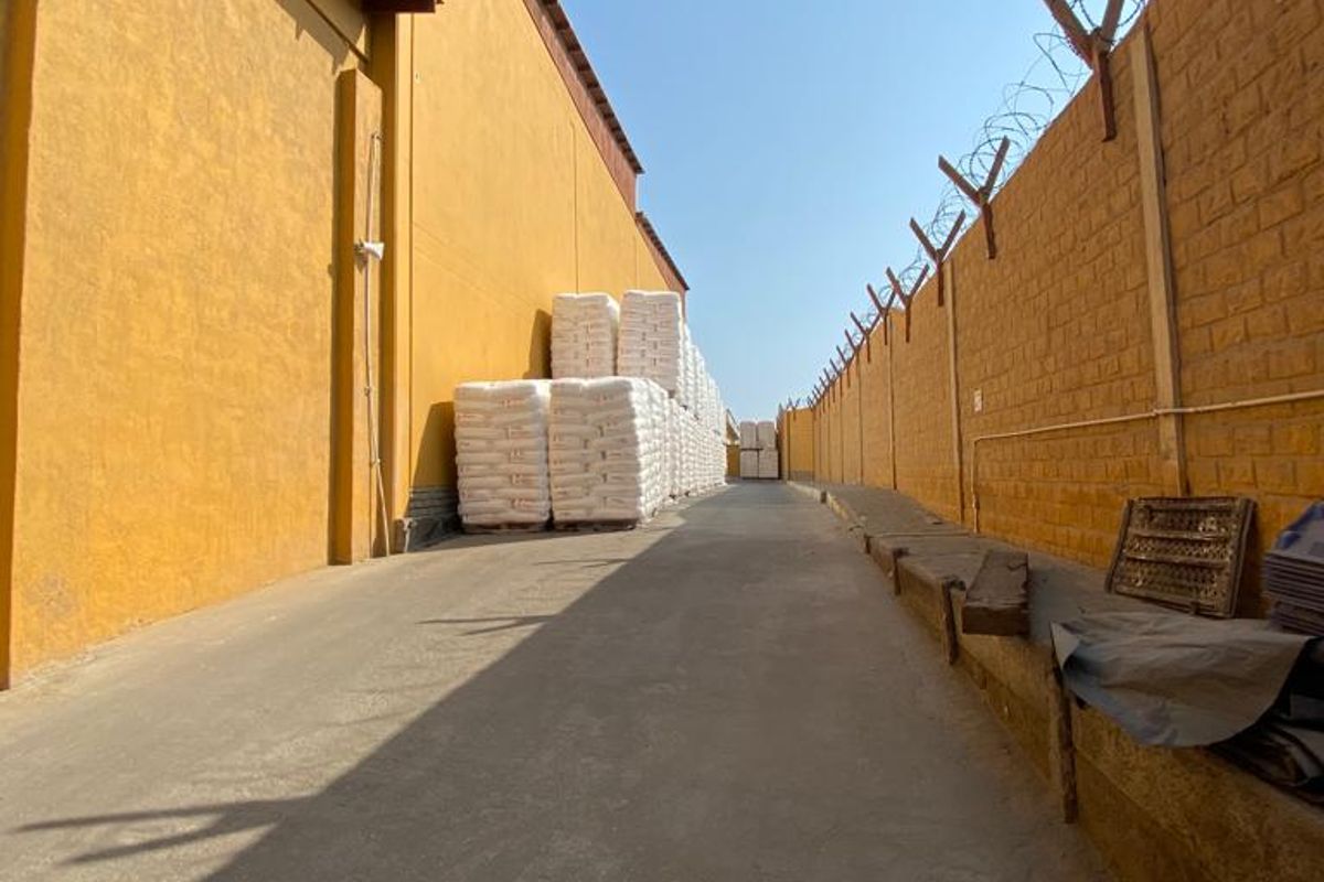 Exterior side yard of an industrial property featuring a paved driveway, high perimeter wall with security razor wire, and industrial storage space.