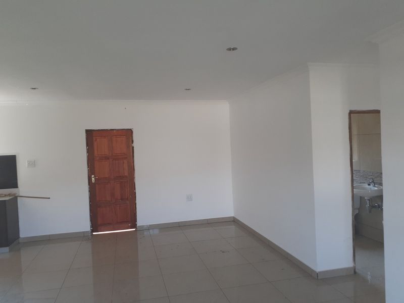 An empty open-plan living area featuring tiled floors, recessed lighting, and access to an adjacent bathroom, presenting a blank canvas for interior design.