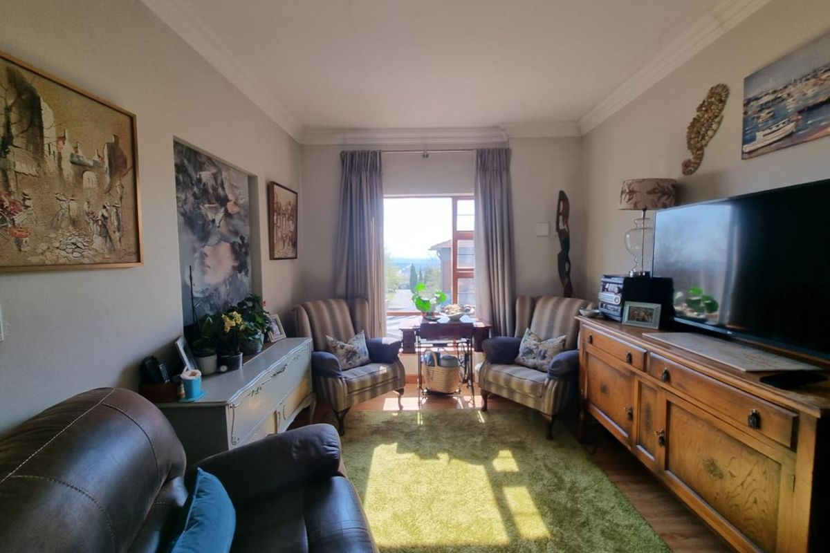 A cozy living room featuring laminate flooring, decorative cornicing, and a window providing natural light and exterior views.