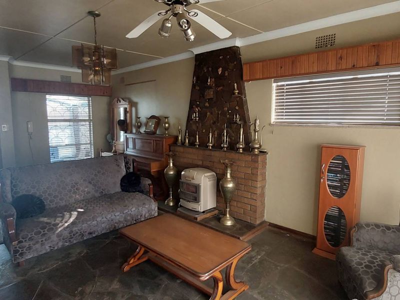 Spacious living room featuring a prominent stone fireplace, natural stone flooring, and timber ceiling accents, offering a traditional aesthetic with potential for modernization.