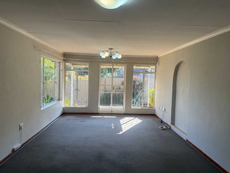 An empty, sunlit living room featuring large windows with security bars, a decorative archway, and neutral wall finishes, ready for new flooring and styling.