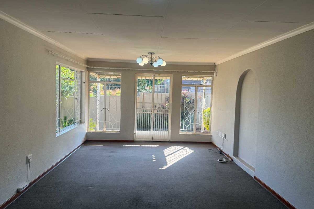 An empty, sunlit living room featuring large windows with security bars, a decorative archway, and neutral wall finishes, ready for new flooring and styling.