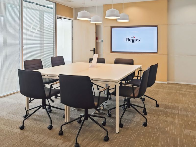 A professional meeting room featuring a built-in display screen, glass partition walls, and carpeted flooring, suitable for corporate office use.
