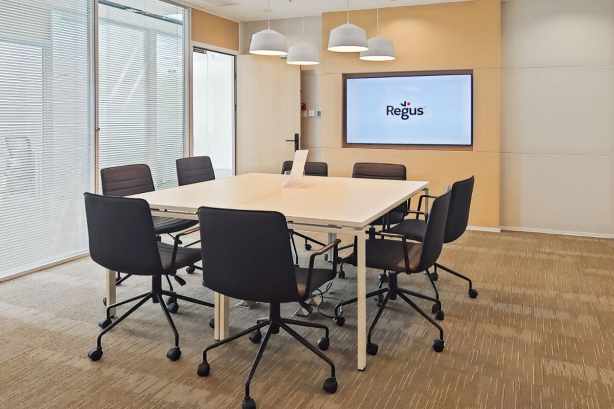 A professional meeting room featuring a built-in display screen, glass partition walls, and carpeted flooring, suitable for corporate office use.