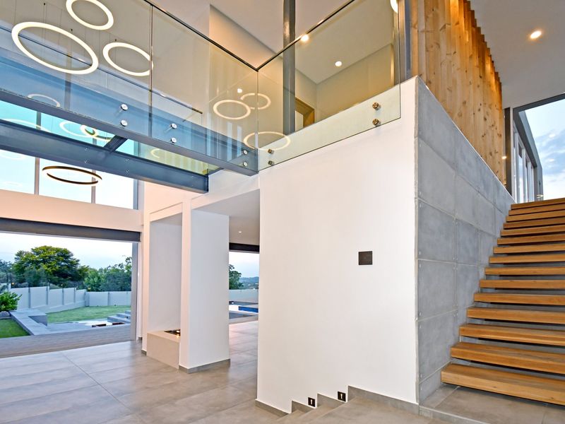 Spacious double-volume living area featuring a modern timber staircase, glass balustrade, concrete feature wall, and large bi-fold doors opening to the garden.