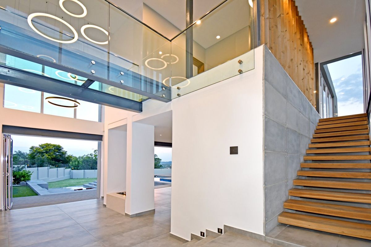 Spacious double-volume living area featuring a modern timber staircase, glass balustrade, concrete feature wall, and large bi-fold doors opening to the garden.