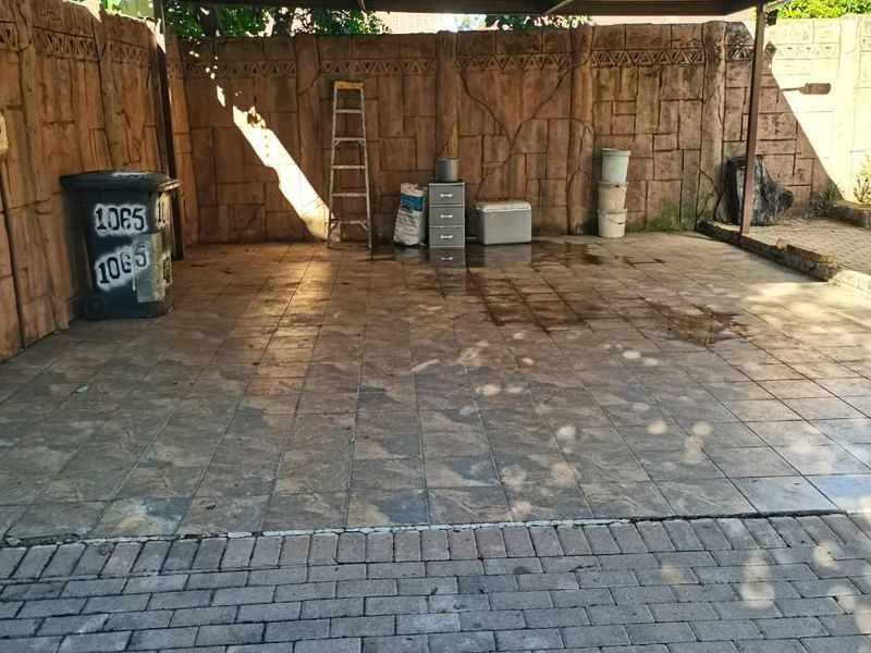 A covered outdoor parking area or garage space featuring tiled flooring, a metal roof structure, and a textured boundary wall.