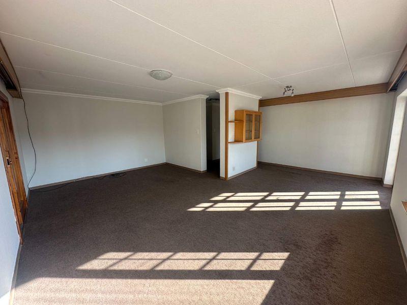 A spacious, empty living area featuring neutral walls, carpet flooring, and a built-in wall cabinet, offering a blank canvas for potential interior updates.