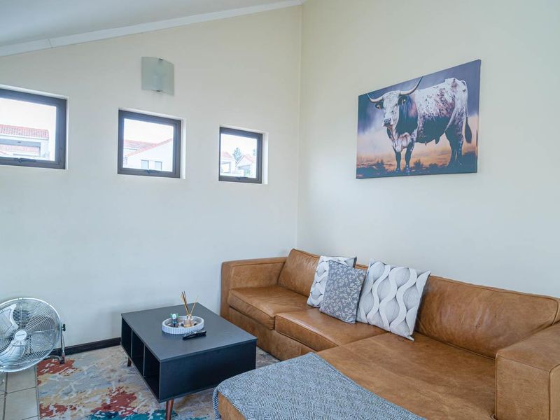 A bright living room featuring a sloped ceiling, three small square windows, and neutral wall finishes.