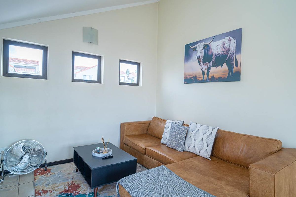 A bright living room featuring a sloped ceiling, three small square windows, and neutral wall finishes.