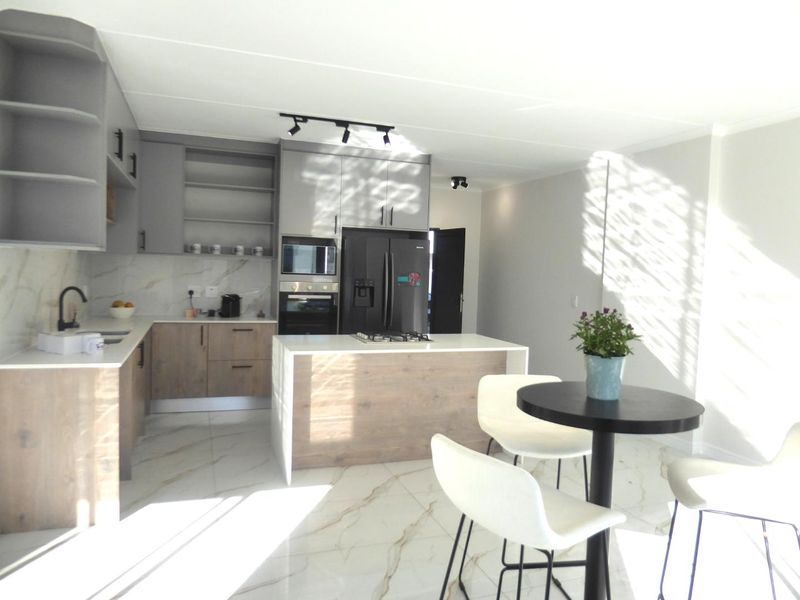 Modern open-plan kitchen featuring two-tone cabinetry, stone countertops, a central island with a gas cooktop, and elegant marble-look floor tiles.