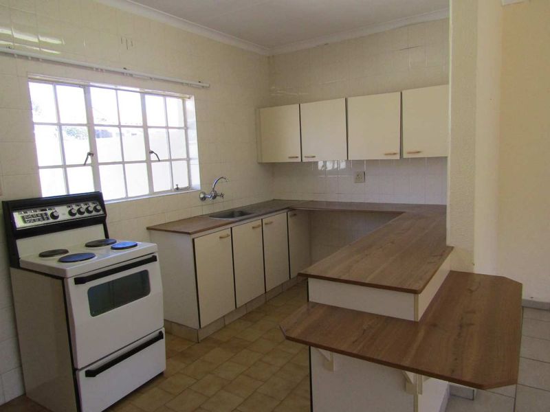 A functional, dated kitchen featuring built-in cabinetry, laminate countertops, a stainless steel sink, and a freestanding stove with tiled splashbacks.
