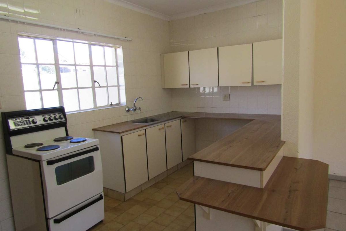 A functional, dated kitchen featuring built-in cabinetry, laminate countertops, a stainless steel sink, and a freestanding stove with tiled splashbacks.