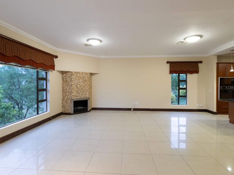 Spacious open-plan living area featuring large windows, tiled flooring, and a stone-clad fireplace, seamlessly flowing into the adjacent kitchen space.