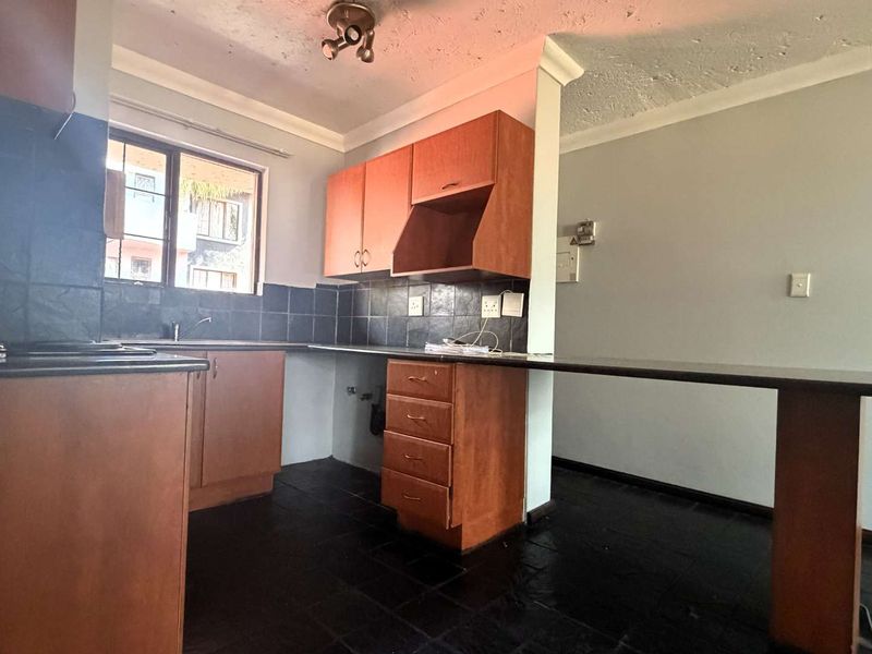 A dated kitchen featuring wooden cabinetry, a breakfast bar, and dark tiled flooring, offering a functional layout ready for modern updates.