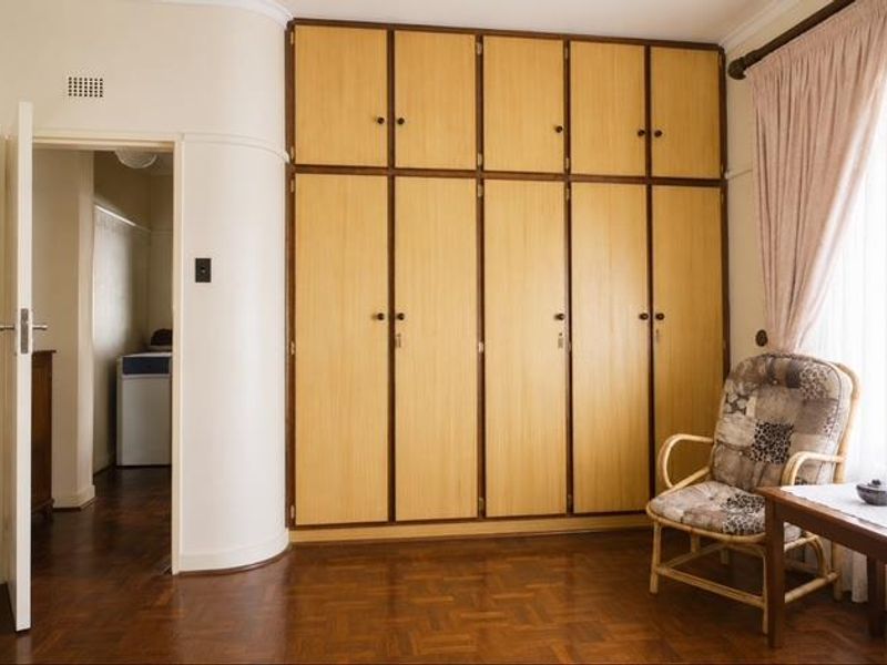 A bedroom featuring classic parquet flooring and extensive floor-to-ceiling built-in wooden cupboards, offering ample storage space.