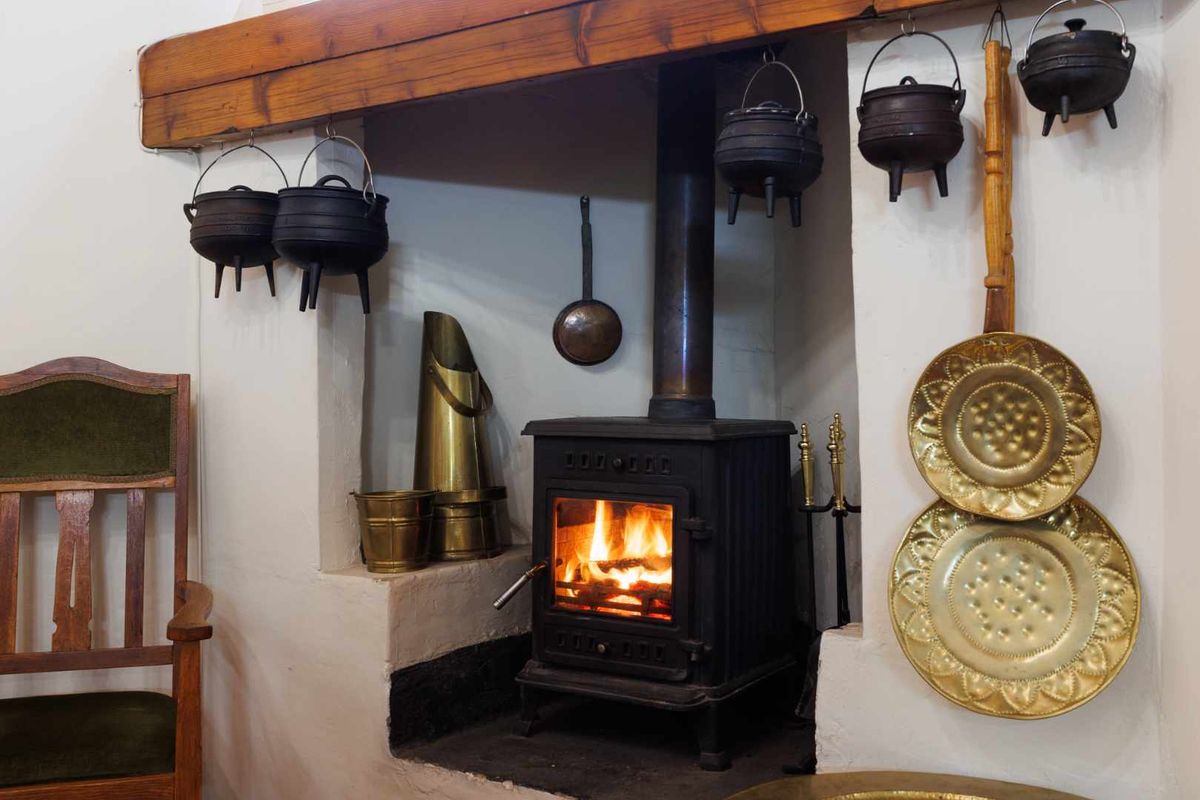 A cozy living room area featuring a traditional cast iron wood-burning stove set within a rustic masonry fireplace with a timber mantelpiece.