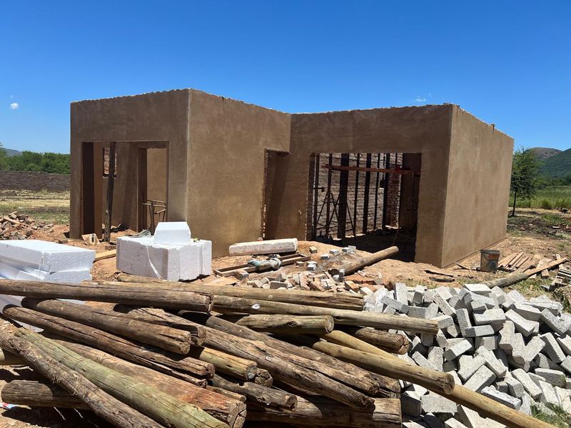 A property currently under construction, featuring raw plastered walls and an open-plan layout, situated on a large plot with building materials on site.