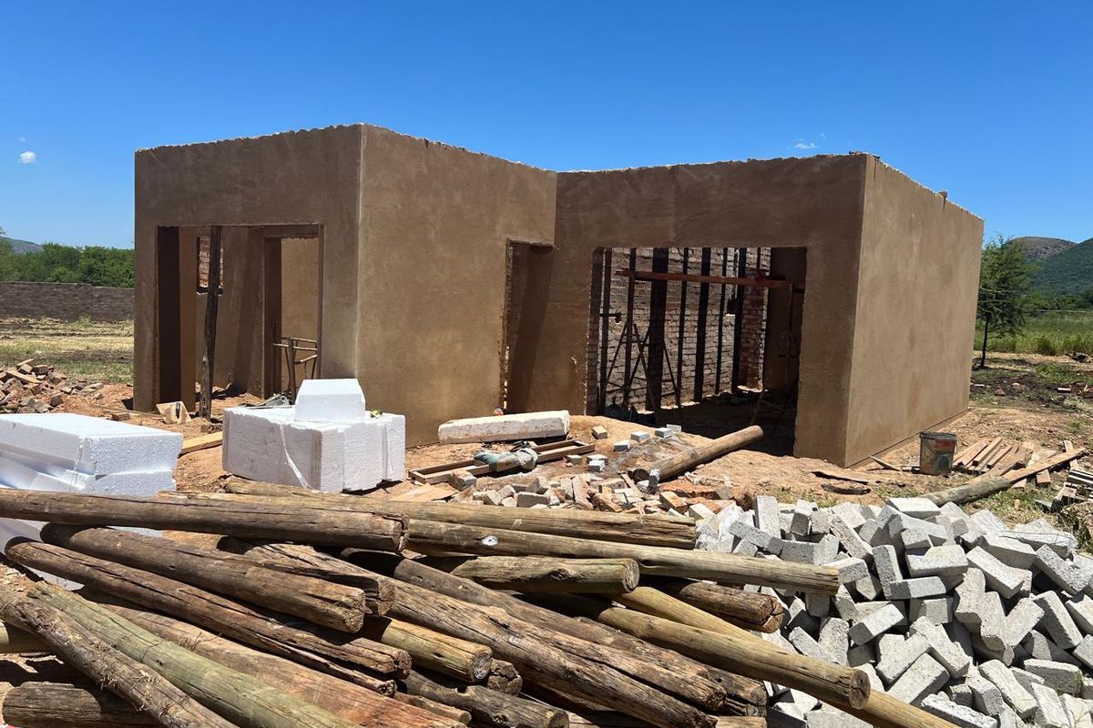 A property currently under construction, featuring raw plastered walls and an open-plan layout, situated on a large plot with building materials on site.