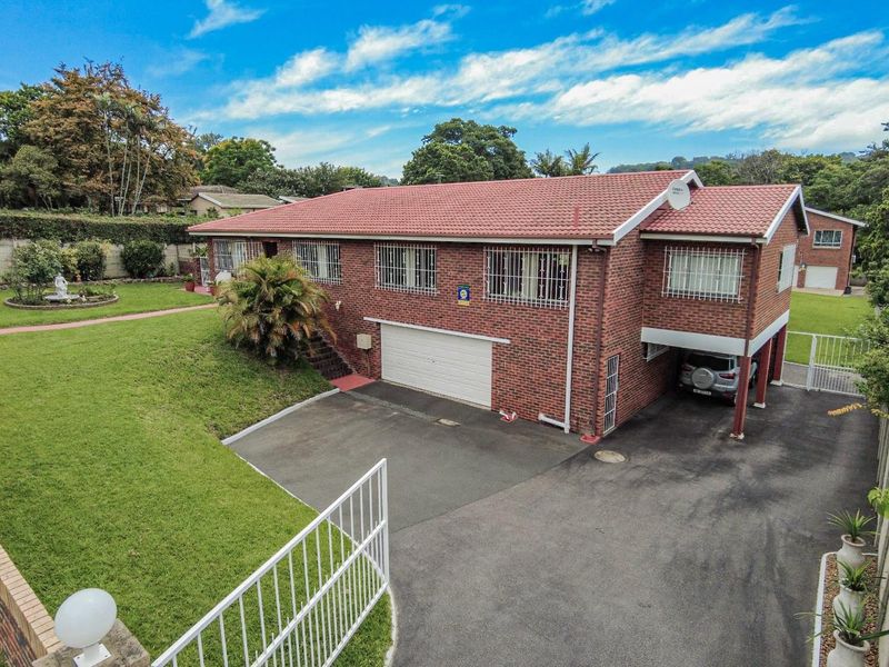 A well-maintained brick house featuring a tiled roof, double garage, carport, and a spacious paved driveway set within a landscaped garden.