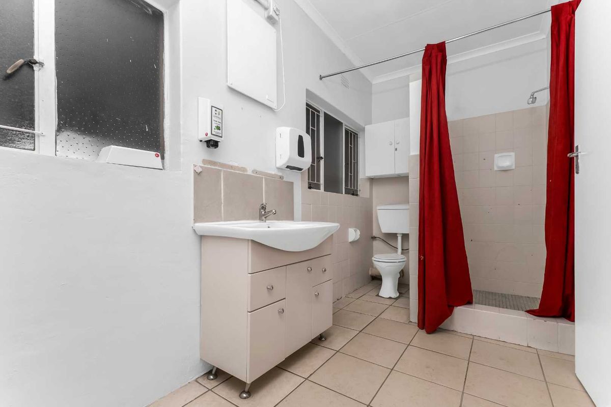 A functional bathroom featuring a vanity unit, toilet, and shower enclosure with tiled finishes, requiring some cosmetic updates to improve its overall condition.
