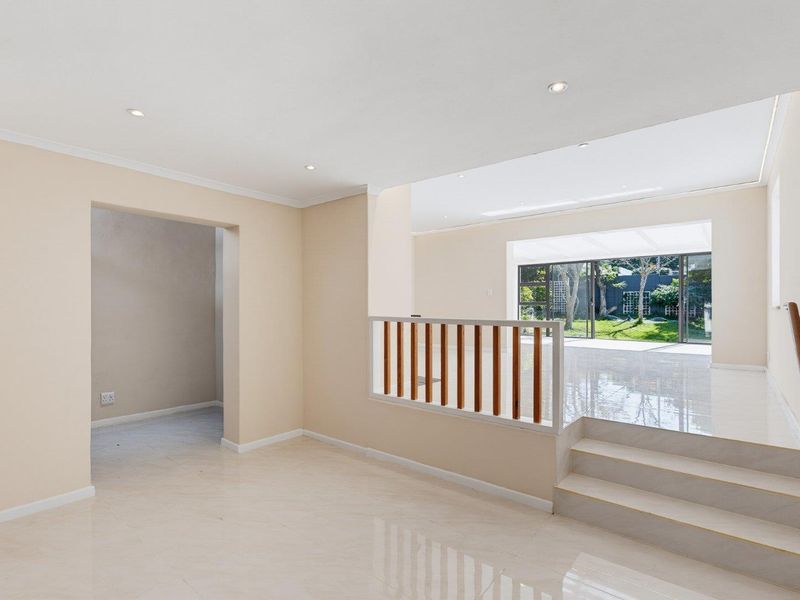 Spacious open-plan living area featuring tiled floors, recessed lighting, a wooden balustrade, and large sliding doors leading to the garden.