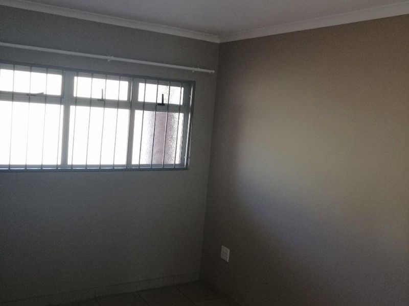 An empty bedroom featuring tiled flooring, neutral walls, and security bars on the window.