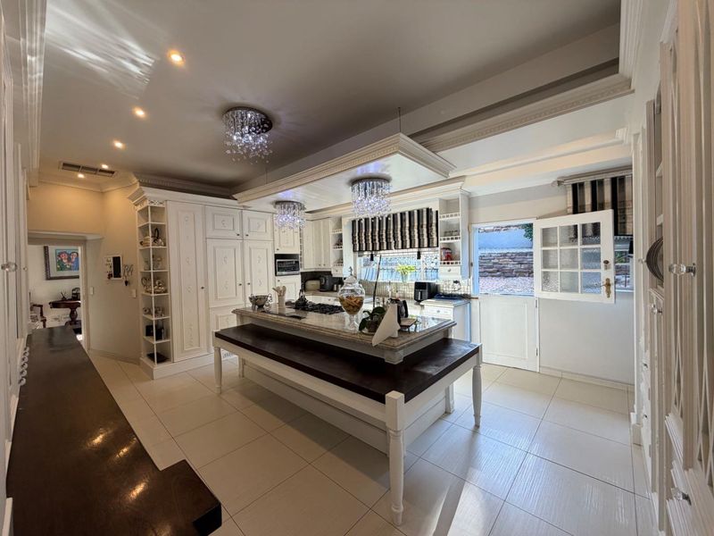 Spacious kitchen featuring a large central island with granite countertops, built-in cabinetry, gas hob, and elegant crystal chandeliers, opening to an outdoor area.
